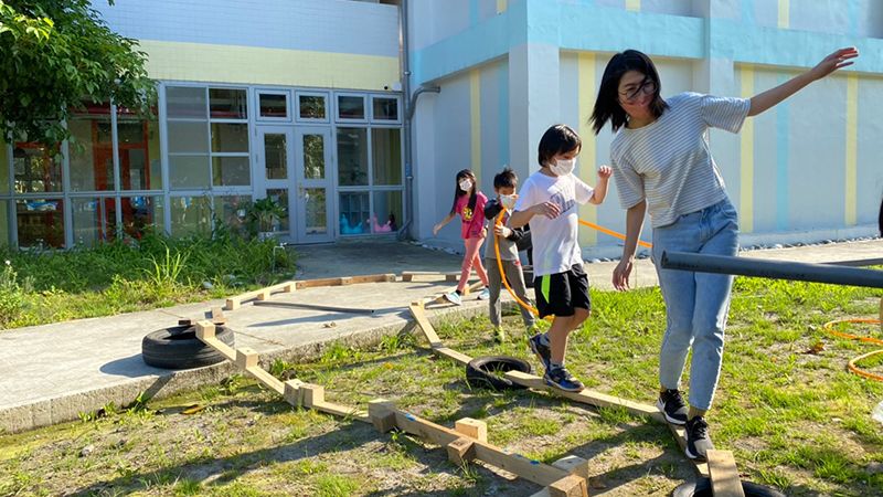 玩轉學校的共玩聚落裡，孩子和大人們一起試走用棧板、輪胎搭建的平衡木。圖片提供：玩轉學校