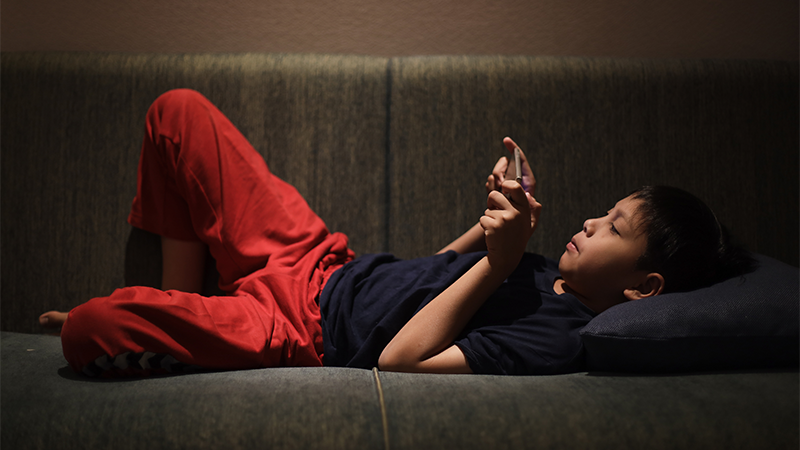 孩子躺在沙發上,沈迷手機遊戲